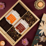 Box of chocolates with floral packaging on a purple surface with candles and flowers.